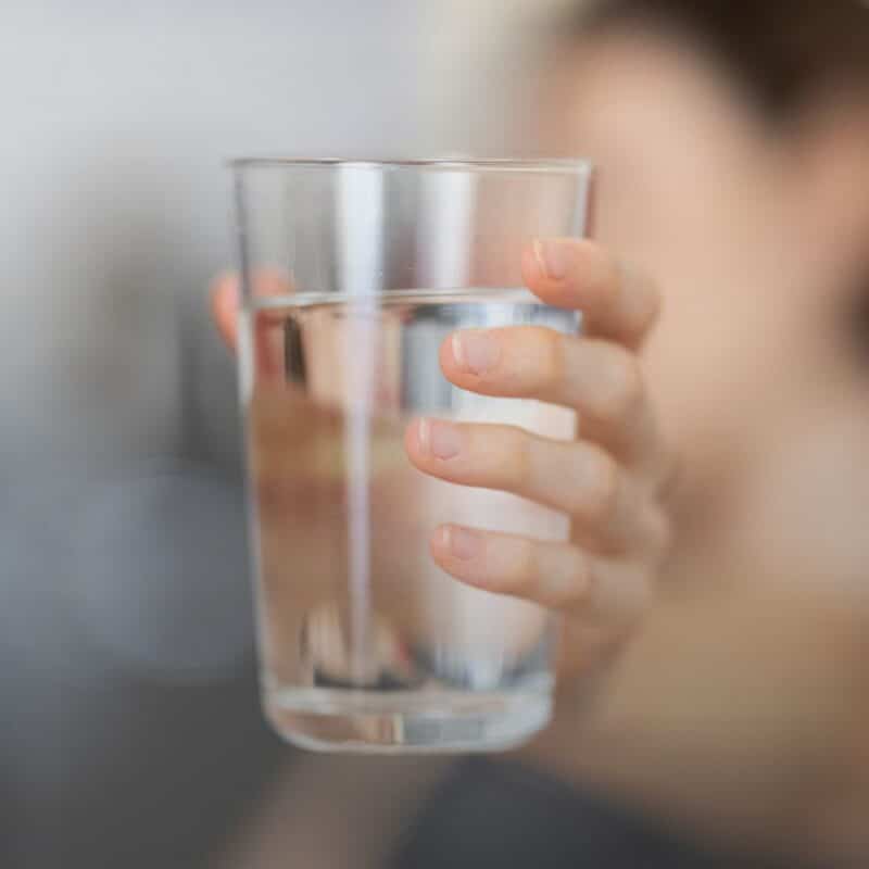 A person holding up a glass of clear, clean drinking water with a soft, blurred background.