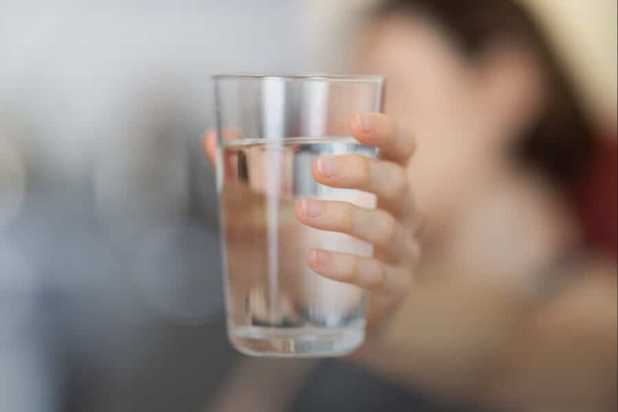 A person holding up a glass of clear, clean drinking water with a soft, blurred background.