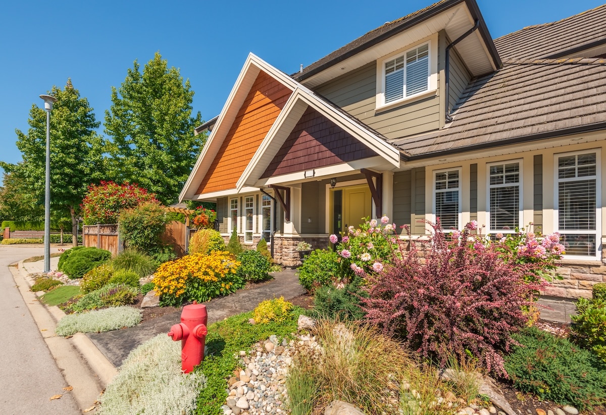 Exterior of a craftsman home featuring multi-colored shingled gables, a yellow front door, and lush front yard garden landscaping next to a red fire hydrant