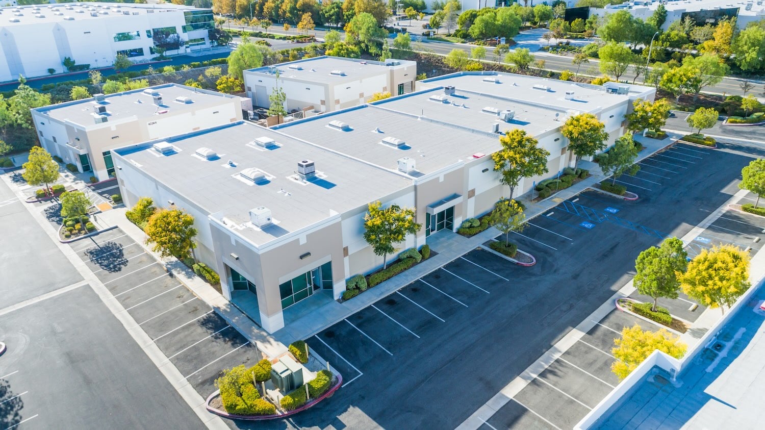 An aerial view of a modern low-rise commercial building complex surrounded by paved parking lots and landscaped trees.