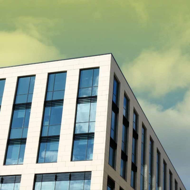 Low-angle view of a modern multi-story commercial building with a white grid facade and large glass windows set against a cloudy sky.