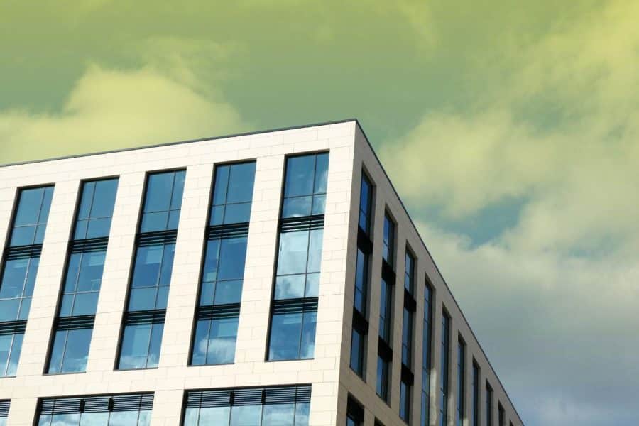 Low-angle view of a modern multi-story commercial building with a white grid facade and large glass windows set against a cloudy sky.