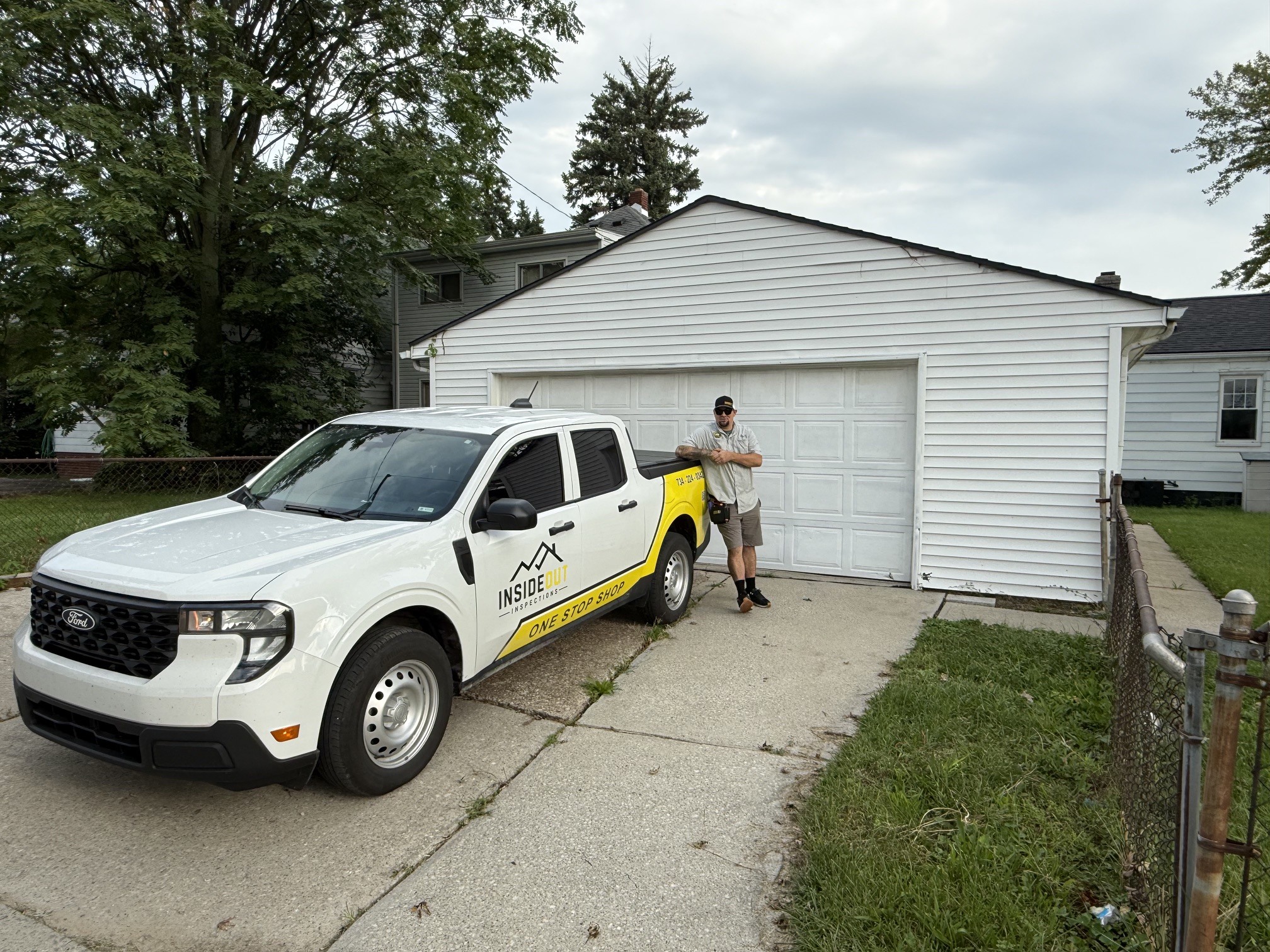 An Inside Out Inspections technician leaning against a white branded truck parked in the concrete driveway of a residential home.