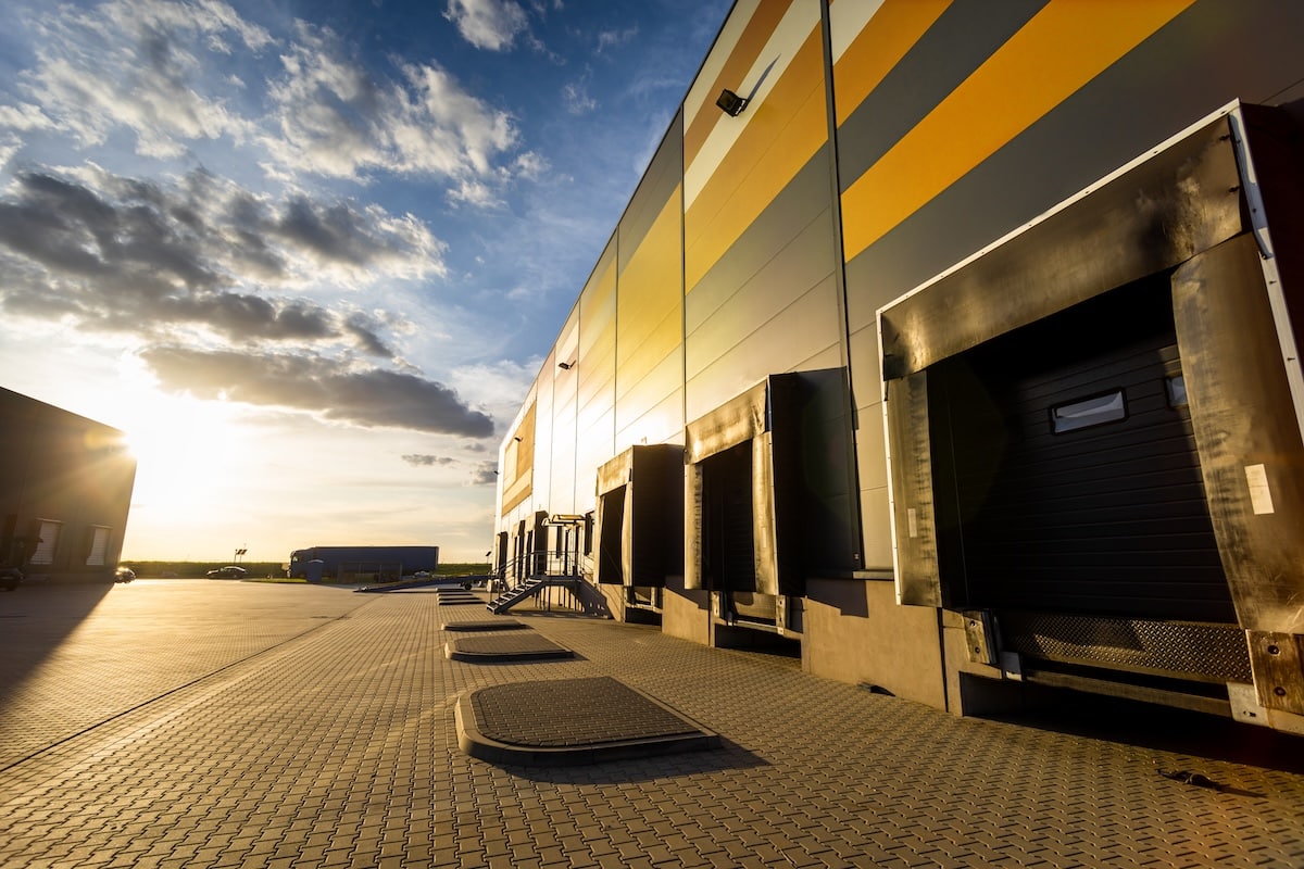 Exterior of a large industrial warehouse building with multiple loading dock bays during sunset.